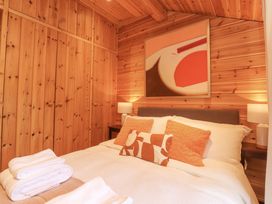 A bedroom with wooden walls a bed with orange and white pillows bedside tables with lamps and folded white towels at Artisan Lodge in Longridge