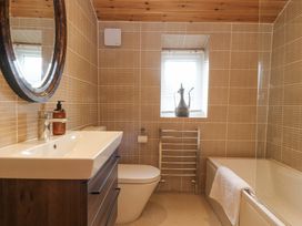 A bathroom with a sink and wooden cabinet a toilet a window with blinds and a decorative vase a towel on a bathtub at Artisan Lodge in Longridge