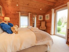 A bedroom with a bed with blue and beige pillows a chair wooden walls and large glass door at Artisan Lodge in Longridge