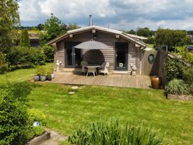 A wooden cabin with a deck patio table umbrella and chairs in a garden at Artisan Lodge in Longridge