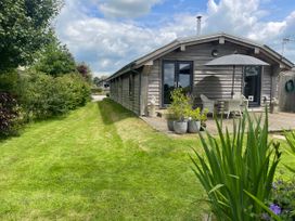 A wooden lodge with patio furniture and umbrella on a deck surrounded by grass and potted plants at Artisan Lodge in Longridge