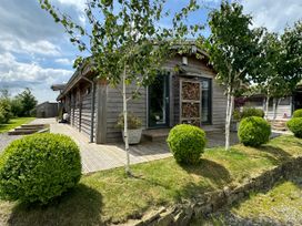 A wooden house with a stacked wood rack outside surrounded by trees and bushes at Artisan Lodge in Longridge