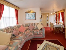 A living room with a patterned sofa and cushions red curtains a wooden dining table with chairs at Meric Stone Holiday lets Caravan 1 Benone near Castlerock