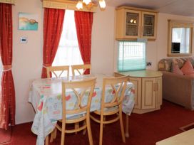 A dining area with a table covered by a tablecloth and four chairs next to windows with red curtains and a seating area with a sofa in Meric Stone Holiday lets Caravan 1 Benone near Castlerock
