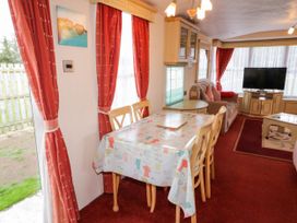 A dining table with chairs and a sofa with cushions in a room with red curtains and a television at Meric Stone Holiday lets Caravan 1 in Benone near Castlerock