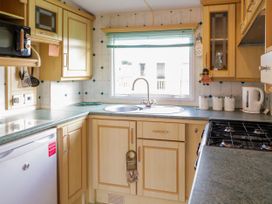 A kitchen with wooden cabinets a gas stove a sink below a window and a kettle on the countertop at Meric Stone Holiday lets Caravan 1 Benone near Castlerock