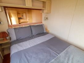 A bedroom with a double bed covered in gray bedding and pillows with a lamp on a bedside table at Meric Stone Holiday lets Caravan 1 in Benone near Castlerock