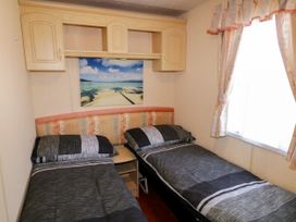 A bedroom with two single beds a small bedside table wooden wall cabinets and a window with curtains at Meric Stone Holiday lets Caravan 1 Benone near Castlerock