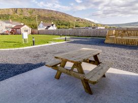 A wooden picnic table on a concrete slab with grass and houses in the background at Meric Stone Holiday lets Caravan 1 in Benone near Castlerock