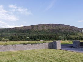 A grassy yard with a stone wall and a mountain in the background at Meric Stone Holiday lets Caravan 1 in Benone near Castlerock