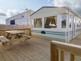 An outdoor wooden deck with a picnic table beside a caravan at Meric Stone Holiday Lets Caravan 2 in Benone near Castlerock