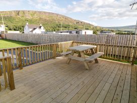 A wooden deck with a picnic table and railing overlooking a fenced yard and hills at Meric Stone Holiday Lets Caravan 2 in Benone near Castlerock