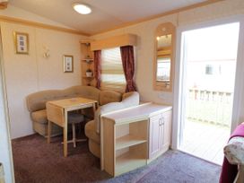 A small dining area with a beige cushioned corner bench and wooden table next to a window with blinds and curtains at Meric Stone Holiday Lets Caravan 2 Benone near Castlerock