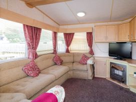 A living room with a beige corner sofa with red cushions curtains around windows a television on a wooden cabinet and a fireplace at Meric Stone Holiday Lets Caravan 2 in Benone near Castlerock