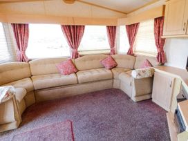 A living room with a beige corner sofa pink curtains and a purple carpet at Meric Stone Holiday Lets Caravan 2 in Benone near Castlerock