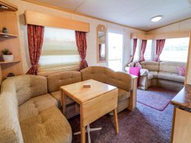 An interior living area with two beige sofas with cushions a small wooden table with foldable sides red curtains and windows at Meric Stone Holiday Lets Caravan 2 Benone near Castlerock