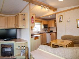 A living area with a television above a heater and kitchen cabinets with a sink and appliances at Meric Stone Holiday Lets Caravan 2 Benone near Castlerock