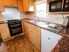 A kitchen with wooden cabinets a black oven a white refrigerator a sink a microwave and a kettle at Meric Stone Holiday Lets Caravan 2 Benone near Castlerock