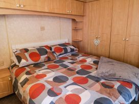 A bedroom with a bed with geometric patterned bedding and wooden wardrobes at Meric Stone Holiday Lets Caravan 2 Benone near Castlerock