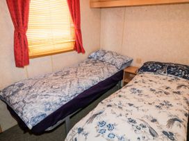 A bedroom with two single beds and red curtains at Meric Stone Holiday Lets Caravan 2 Benone near Castlerock