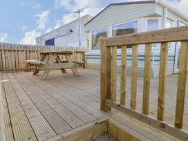 An outdoor wooden deck area with a picnic table and railing next to a caravan at Meric Stone Holiday Lets Caravan 2 Benone near Castlerock
