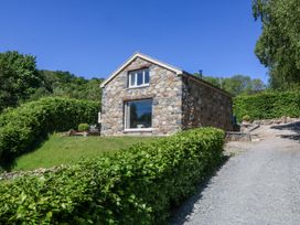 A stone house with a large window and green hedges along a gravel driveway at Holly Cottage in Llechwedd near Conwy