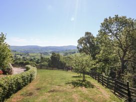 A grassy garden area with hedges and wooden fences overlooking rolling hills and trees at Holly Cottage in Llechwedd near Conwy