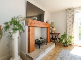 A fireplace with wooden mantel and metal grate next to a plant on a pedestal and a side table with a lamp at Holly Cottage in Llechwedd near Conwy