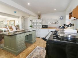 A kitchen with a green island, black stove, white cabinets, a plate rack and a microwave at Holly Cottage in Llechwedd near Conwy