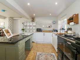 A kitchen with a green island countertop white cabinets black stove and shelves with dishes at Holly Cottage in Llechwedd near Conwy