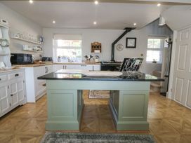 A kitchen with a central green island with black countertop a window stove and shelves with kitchenware at Holly Cottage in Llechwedd near Conwy