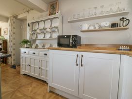 A kitchen with white cabinets a microwave plates cups glasses and a potted plant at Holly Cottage in Llechwedd near Conwy