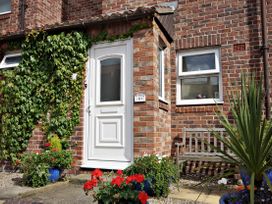 Entrance of a brick house with a white door surrounded by plants and a wooden bench nearby at New Tower House- 10 Pear Tree Court in York