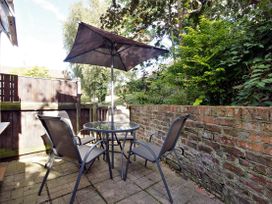 An outdoor patio with a glass table four chairs and an umbrella surrounded by a brick wall and greenery at New Tower House- 10 Pear Tree Court in York