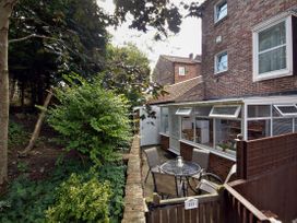 A small patio area with a glass table and chairs next to a brick house with a conservatory and garden in the background at New Tower House 10 Pear Tree Court York