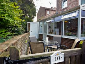 A small outdoor patio area with a round glass table and four chairs next to a brick wall and windows at New Tower House 10 Pear Tree Court York