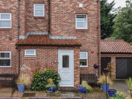 A brick house entrance with a white door and small windows with blue plant pots and benches outside at New Tower House- 10 Pear Tree Court in York