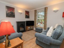 A living room with two blue sofas, a fireplace, a television on a wooden stand, a window with floral curtains, and a red lamp at New Tower House- 10 Pear Tree Court in York