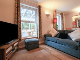 A living room with a blue sofa white pillows a blue ottoman wooden TV stand with a flat screen TV and windows with patterned curtains at New Tower House- 10 Pear Tree Court in York