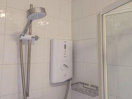 A shower area with a handheld showerhead mounted on a rail a white electric shower unit and a metal wire shelf at New Tower House- 10 Pear Tree Court in York