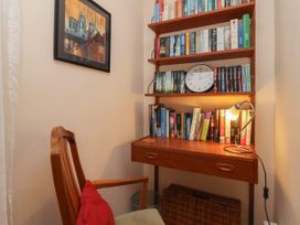 A small reading nook with a wooden chair and a red cushion next to a wooden wall-mounted desk and shelves filled with books and a clock at New Tower House- 10 Pear Tree Court in York
