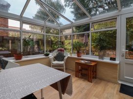 A conservatory with glass roof and windows with plants on the windowsill a table covered with a cloth a wicker chair and nesting tables at New Tower House 10 Pear Tree Court York