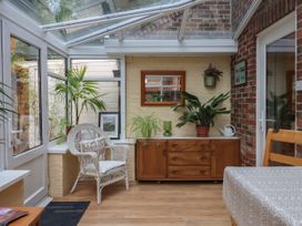 A sunroom with a white wicker chair a wooden sideboard with plants and a mirror at New Tower House- 10 Pear Tree Court in York