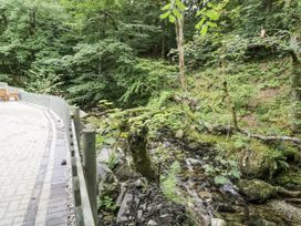 A pathway beside a stream with trees and seating area at Frongoch Old Power House in Dolgellau