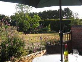 A garden with flowers and a table with a wine bottle and glass at The Cartshed in Defford