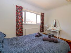 A bedroom with a bed covered in gray bedding and towels on it a dressing table with a round mirror and a standing fan near the window at Cedar View in Hainford near Coltishall