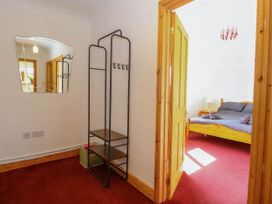 A hallway with a metal coat rack and a mirror next to a doorway leading to a bedroom with a wooden bed and red carpet at Cedar View in Hainford near Coltishall