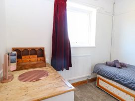 A small bedroom with a single bed with towels on it a wooden desk with a mirror and a small shelving unit under a window with a red curtain at Cedar View in Hainford near Coltishall