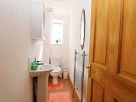 A narrow bathroom with a wooden door a pedestal sink with soap dispenser a toilet a small window a wall cabinet a mirror and a towel radiator at Cedar View in Hainford near Coltishall