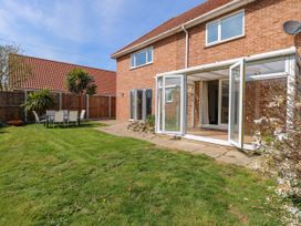 A backyard with grass a patio area with outdoor dining furniture and a house with large glass doors at Cedar View in Hainford near Coltishall